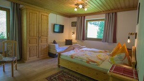 A wooden-paneled bedroom with a bed, a chair, a wardrobe, a television, and a window with curtains. - 110m² vacation apartment in a quiet location in the wild and romantic Zillertal valley (Mayrhofen)