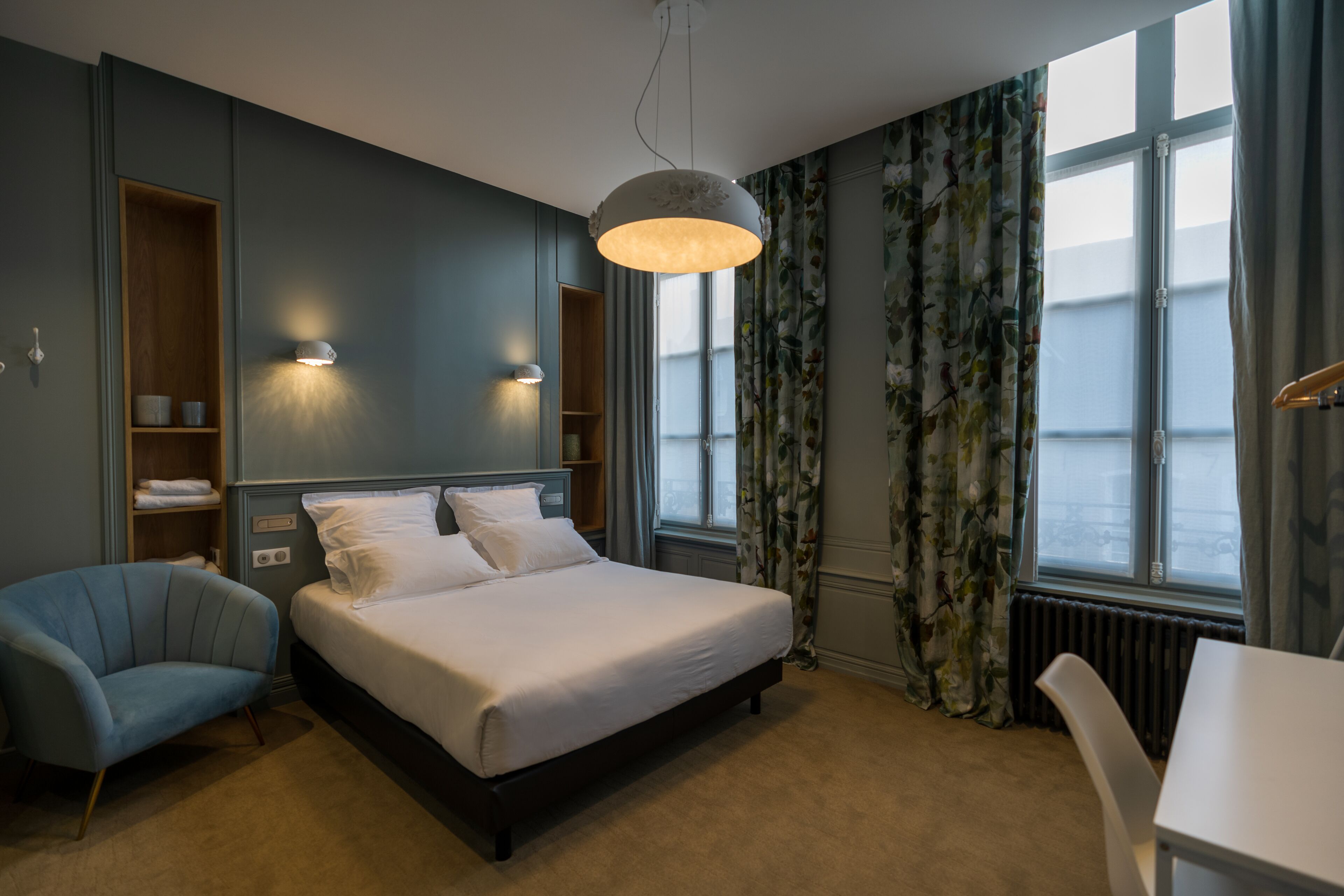 Habitación de hotel moderna con una cama grande, una silla, un escritorio, un armario y vistas de la ciudad a través de la ventana.