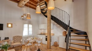Een ruime woonkamer met een houten trap, een eettafel met stoelen en een gezellige zithoek.