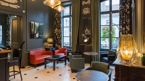 Een hotellobby met een rode bank, ronde tafels en hangende pendantlampen.