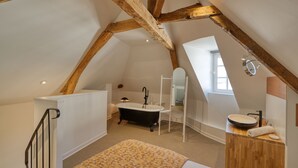 Een slaapkamer met een bed, een houten hoofdeinde, een raam en een badkamer met bad en wastafel.