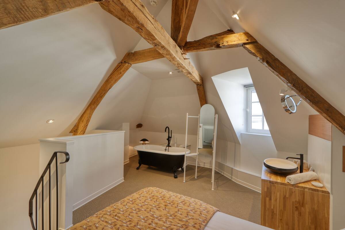 Un dormitorio con cama, cabecera de madera, ventana y baño con bañera y lavamanos.