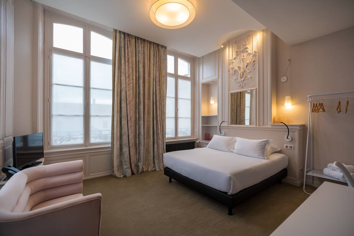 Habitación de hotel con una cama grande, un escritorio, una silla, un televisor y una ventana con cortinas.