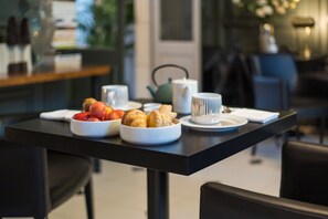 Una mesa de desayuno con cruasanes, un bol de fruta y una tetera.