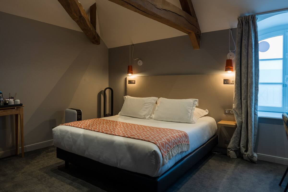 Un dormitorio con cama, mesitas de noche, un escritorio y una ventana con cortinas.