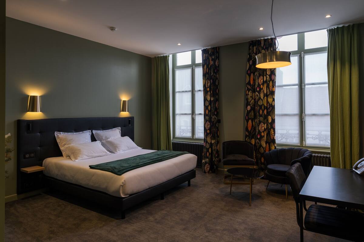 Habitación de hotel con una cama grande, dos lámparas de noche, un escritorio con una silla y vistas a la ciudad a través de la ventana.
