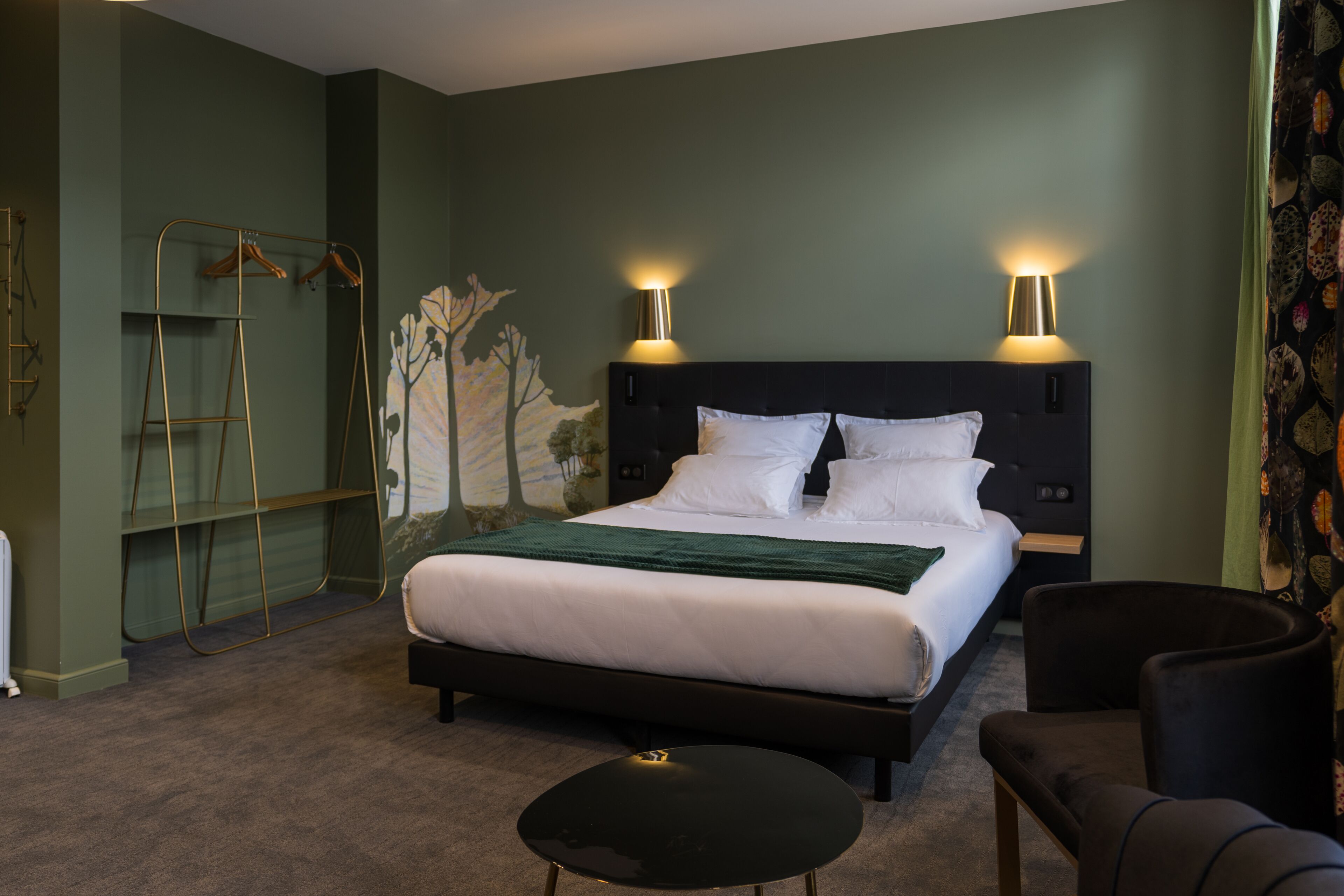A neatly arranged hotel room with a bed, two bedside lamps, a small round table, a chair, and a ladder against the wall.