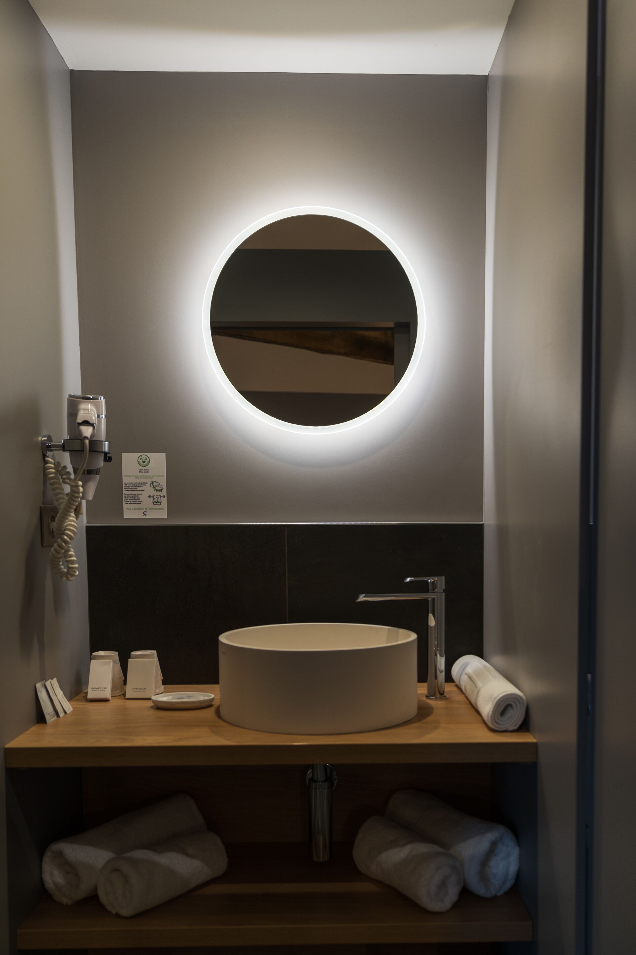 Een moderne badkamer met een ronde spiegel, een wastafel en een handdoekrek.