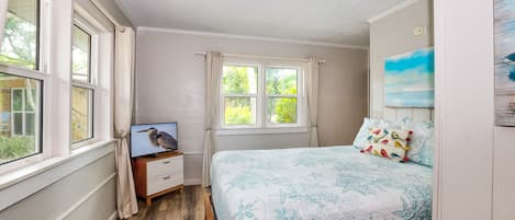 A bedroom with a bed, a TV on a wooden dresser, and a window with curtains.