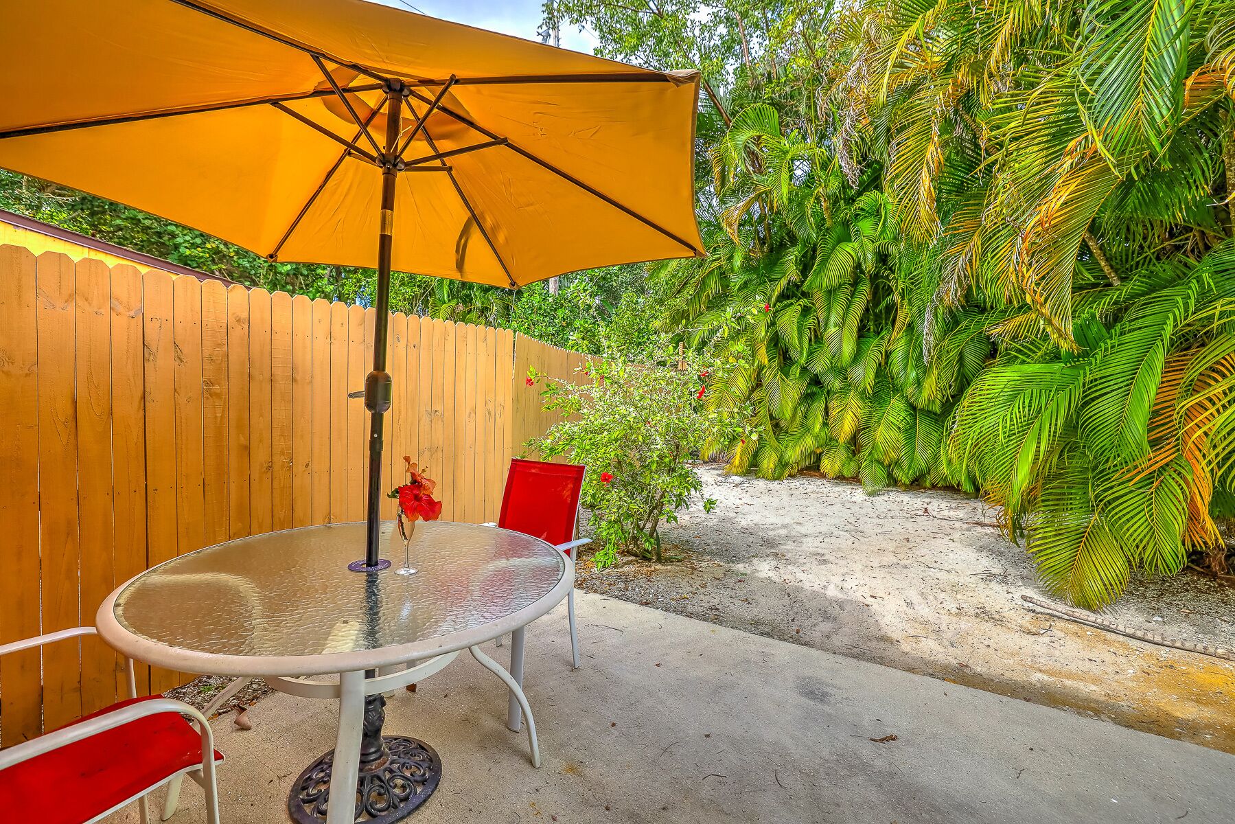 A patio with a glass table, red chairs, and a yellow umbrella.