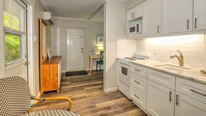 A modern kitchen with white cabinets, a stove, and a microwave. There is a wooden chair and a dining table in the adjacent dining area. - Newly remodeled Parakeet cottage!  Walking distance to beach, restaurants, shops! (Sanibel)