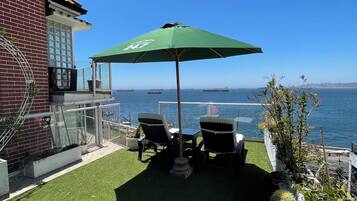 Une terrasse avec du gazon synthétique, un parasol vert et deux chaises.