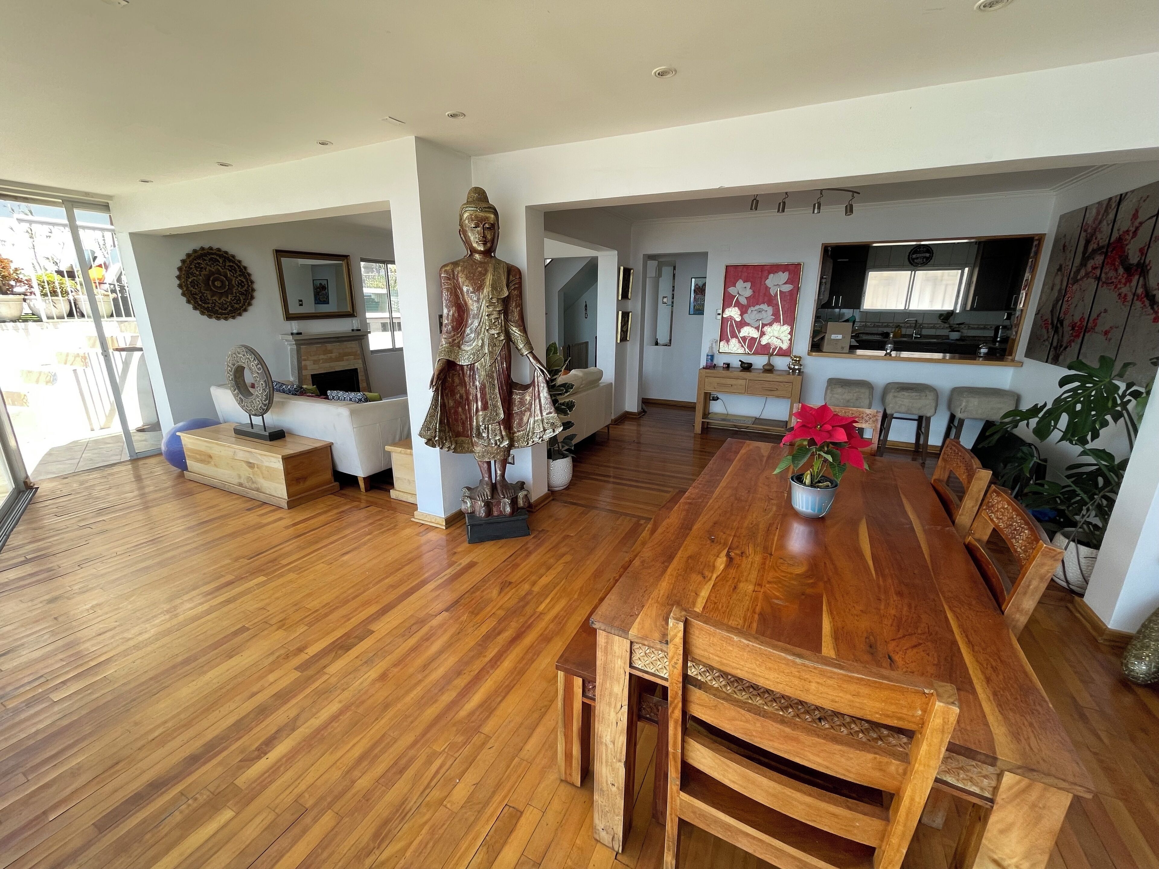 A spacious living room with a wooden dining table, a Buddha statue, and a kitchen area with bar stools.