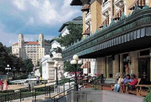 Stroll through the historic public square, surrounded by trees and ornate architecture, featuring a balcony and a statue in the foreground.
