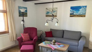 En stue med en rød lænestol, en grå sofa, et træsofabord og to vægmonterede lamper.