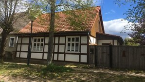 Et traditionelt bindingsværkshus med rødt tegltag, træhegn og en klar himmel.