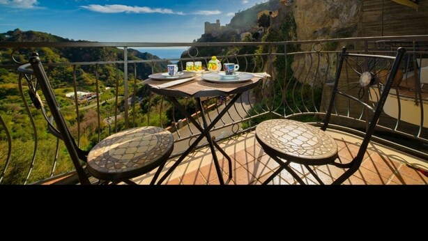 A terrace with a table set for two, overlooking a scenic landscape with a clear sky and distant hills. - Brand new apartment adjacent to the famous Vitelli bar from the film IL PADRINO. (Savoca)