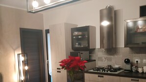 A modern kitchen with a dining area, featuring a wooden table, black chairs, a potted plant, and built-in appliances. - Brand new apartment adjacent to the famous Vitelli bar from the film IL PADRINO. (Savoca)