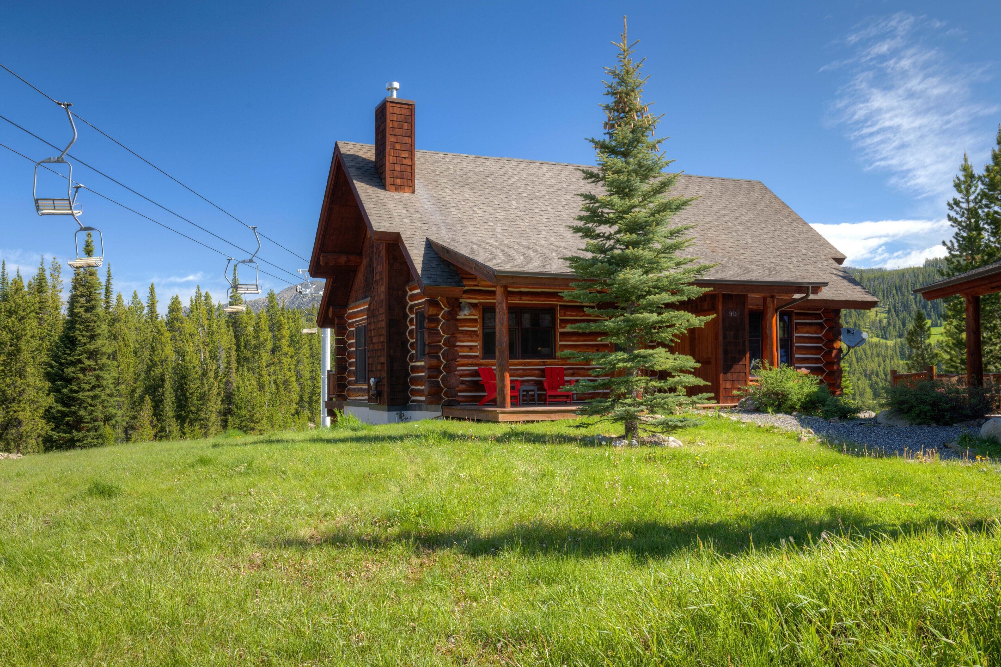 A log cabin with a chimney, wooden porch, and a view of the surrounding forest.