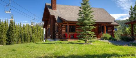 A log cabin with a chimney, wooden porch, and a view of the surrounding forest.