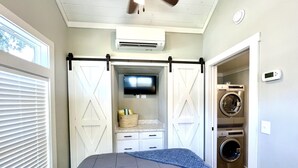 A bedroom with a bed, a TV, a washing machine, and a laundry room.