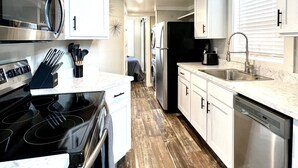 A modern kitchen with stainless steel appliances, white cabinetry, and a wooden floor.