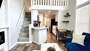 A spacious living area with a staircase leading to a loft, a kitchen with modern appliances, and a cozy seating area with a blue sofa.