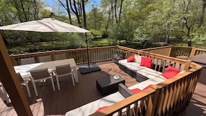 A wooden deck with a table, chairs, a sofa with red cushions, and a large umbrella.