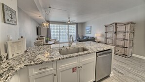 A modern kitchen with granite countertops, a built-in dishwasher, and a large window.