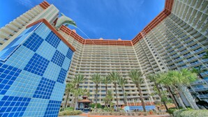 A high-rise hotel with multiple floors, a central courtyard with palm trees, and a clear blue sky.