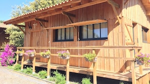 Une cabane en bois dotée d’un toit à pente, de grandes fenêtres et d’une terrasse en bois agrémentée de jardinières suspendues.