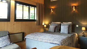 Une chambre à coucher aux murs lambrissés, avec un lit, deux lampes de chevet, un radiateur et une fenêtre avec des rideaux.