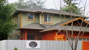 A two-story house with a sign that reads "Robin's Nest" and a fenced garden with various plants and flowers. - Heron's Perch Efficiency Studio (Port Townsend)