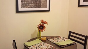 A dining table with a framed picture above it, a vase with flowers, and a placemat. - Heron's Perch Efficiency Studio (Port Townsend)