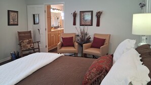 A bedroom with a bed, two chairs, a dresser, a mirror, and a vase with dried flowers. - Heron's Perch Efficiency Studio (Port Townsend)