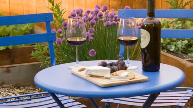 A round table with a bottle of wine, two glasses of wine, a cheese board with grapes, and a vase of purple flowers. - Heron's Perch Efficiency Studio (Port Townsend)