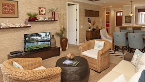 A living room with wicker furniture, a flat-screen TV, and decorative items on the wall. - Luxury Zen Polynesian Penthouse (Waikoloa Resort)