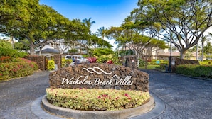 A stone sign with the text "Waikoloa Beach Villas" surrounded by a landscaped area with various plants and flowers. - Luxury Zen Polynesian Penthouse (Waikoloa Resort)