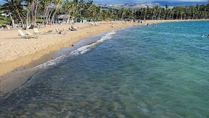 A beach with clear water, palm trees, and a few people swimming. - Luxury Zen Polynesian Penthouse (Waikoloa Resort)