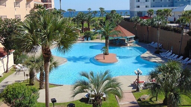 A resort with a large central pool, palm trees, and a view of the ocean. - Beach Therapy at Maravilla by My Galveston Getaway (Galveston)