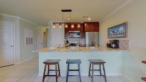 A kitchen with a central island, wooden cabinets, a stainless steel refrigerator, and a coffee maker. - Beach Therapy at Maravilla by My Galveston Getaway (Galveston)