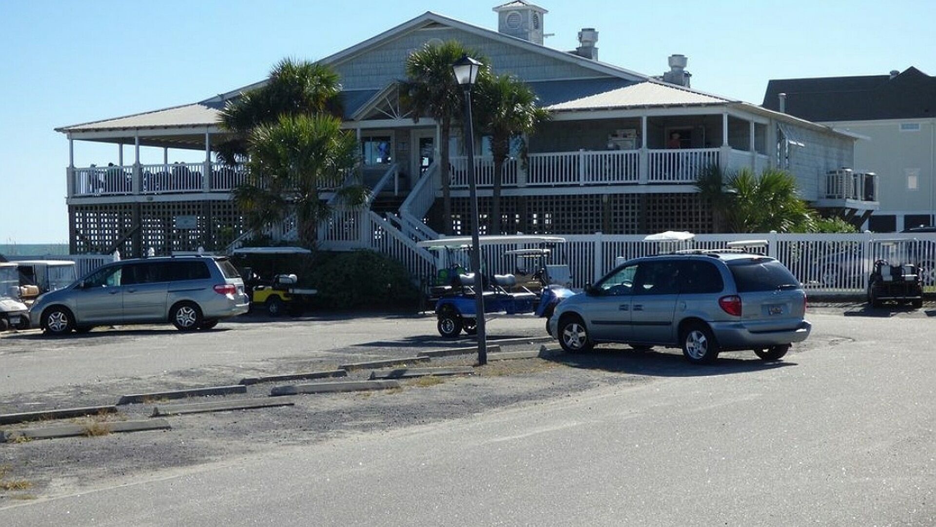 Un grand immeuble doté d’un balcon, d’un escalier et d’un parking où sont garées plusieurs voitures.