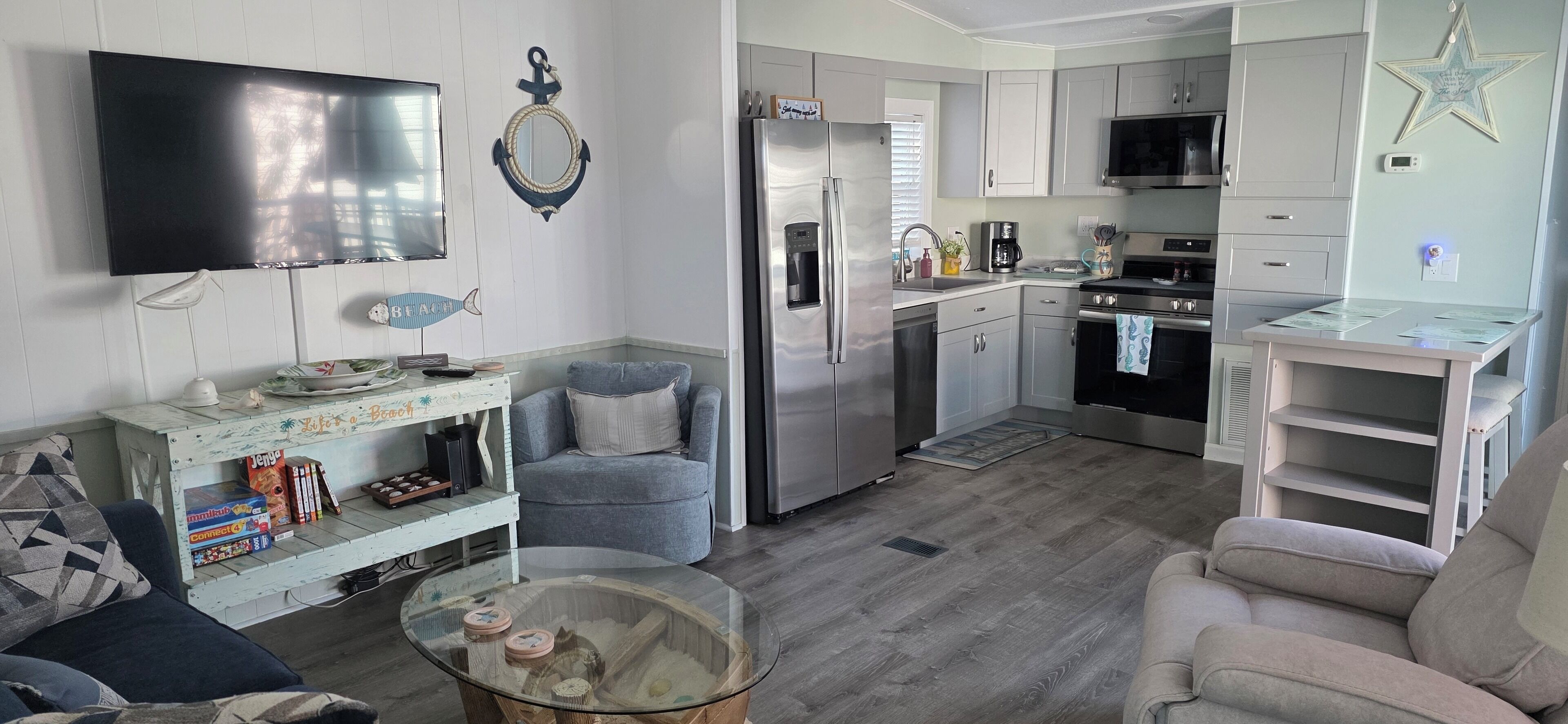 A modern kitchen with a refrigerator, microwave, and stove. There is a dining table and a sofa in the living area.