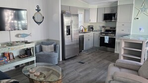 A modern kitchen with a refrigerator, microwave, and stove. There is a dining table and a sofa in the living area. - CLEAN , Pet Friendly Beach House w/ golf cart and free beach parking (Surfside Beach)