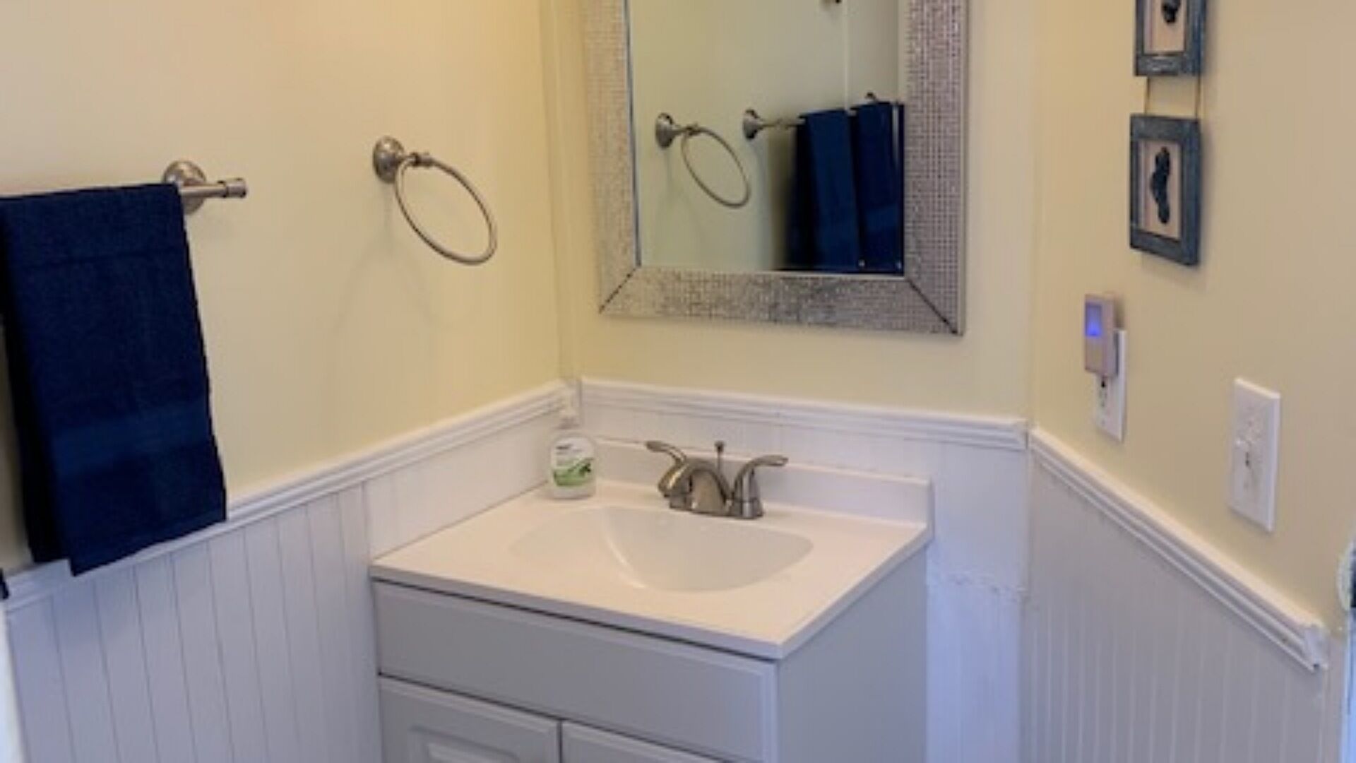 A bathroom with a white sink, a mirror, a towel ring, and a framed picture on the wall.