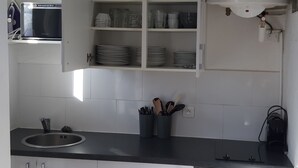 A kitchen with white cabinets, a black countertop, and a built-in microwave. - Studio in the center of Juan-les-pins (Antibes)