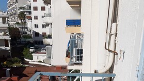 A balcony with a metal table and chairs, a railing, and a view of buildings and parked cars. - Studio in the center of Juan-les-pins (Antibes)