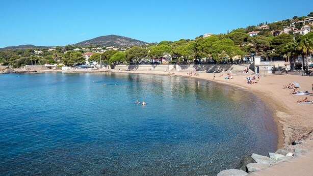 Una spiaggia costiera con acqua cristallina, una riva sabbiosa e edifici sullo sfondo.