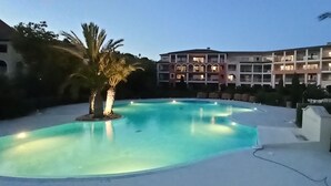Una piscina con una palma al centro, circondata da sdraio. Sullo sfondo, un edificio a più piani con balconi.