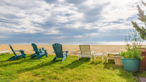 En græsplæne med flere Adirondack-stole, der vender ud mod stranden.